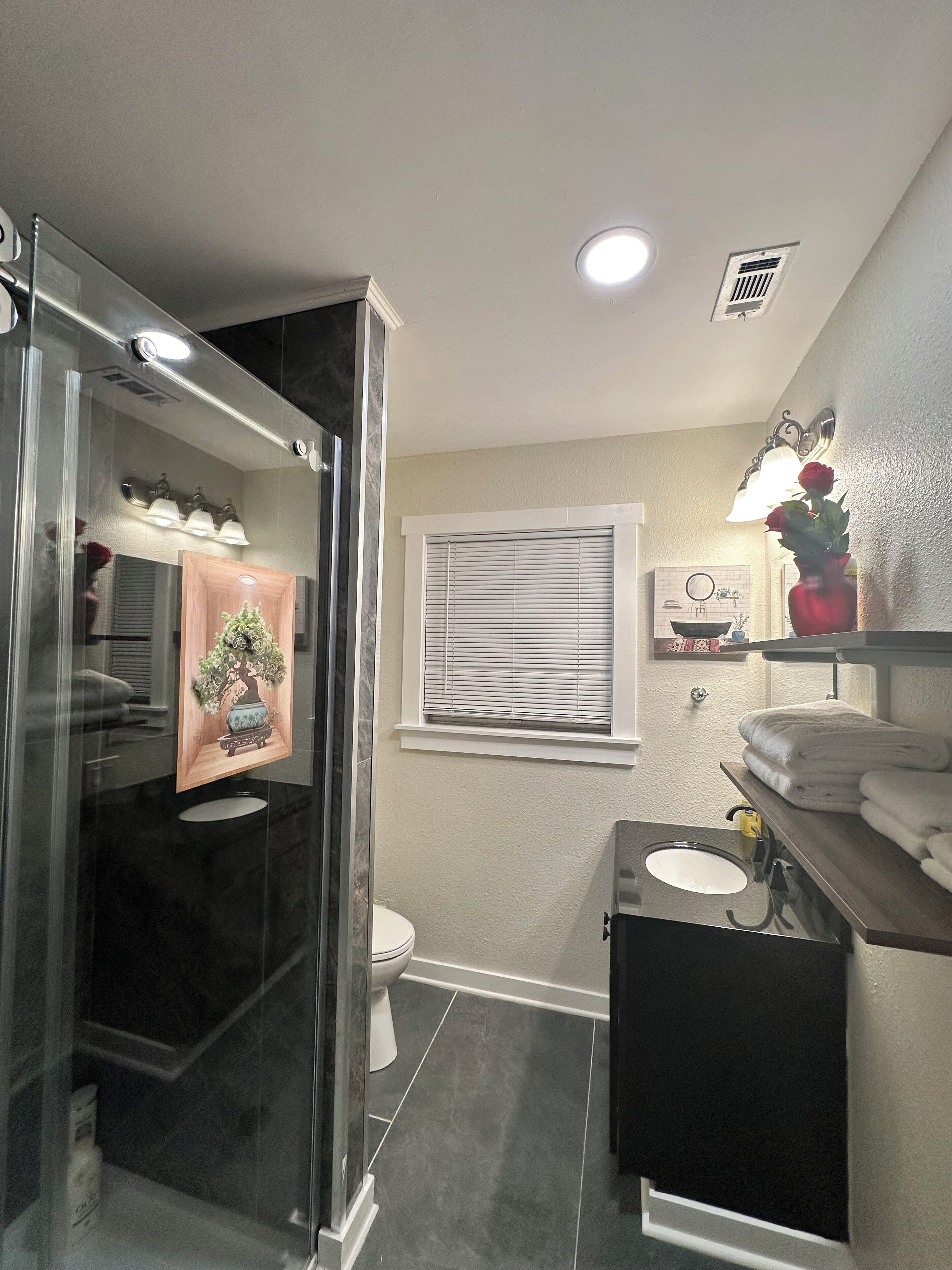 A modern bathroom with a glass shower enclosure, a toilet, a sink, and a vanity with towels.