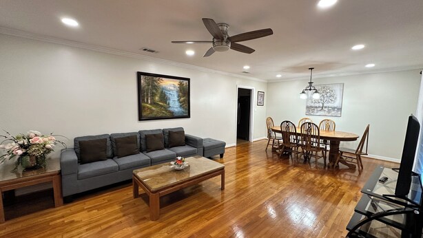 A living room with a gray sofa, wooden coffee table, dining table with chairs, a ceiling fan, and a painting on the wall. - Happily Ever Home in Pensacola (Pensacola)