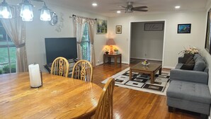 A living room with a wooden dining table, chairs, a grey sofa, a coffee table, and a TV. - Happily Ever Home in Pensacola (Pensacola)