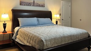 A bedroom with a bed, two bedside lamps, a ceiling fan, a door, and a cityscape painting on the wall. - Happily Ever Home in Pensacola (Pensacola)