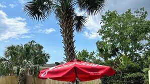 A backyard with a swimming pool, a palm tree, and a red umbrella table. - Happily Ever Home in Pensacola (Pensacola)