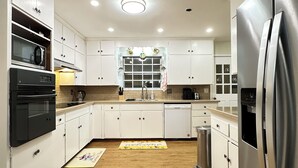 A modern kitchen with white cabinets, stainless steel appliances, and a wooden floor. - Happily Ever Home in Pensacola (Pensacola)