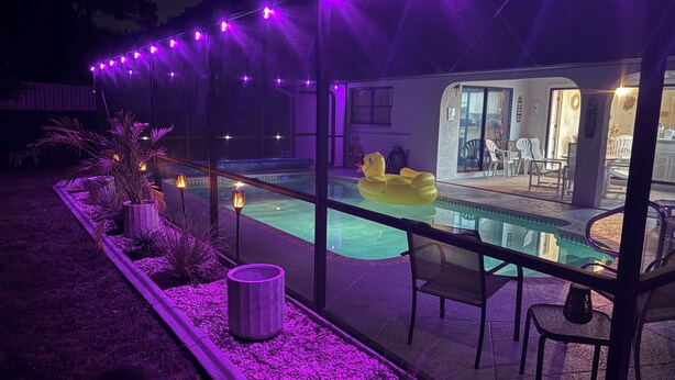 Zona de piscina con barandilla de vidrio, asientos exteriores y un flotador inflable amarillo.