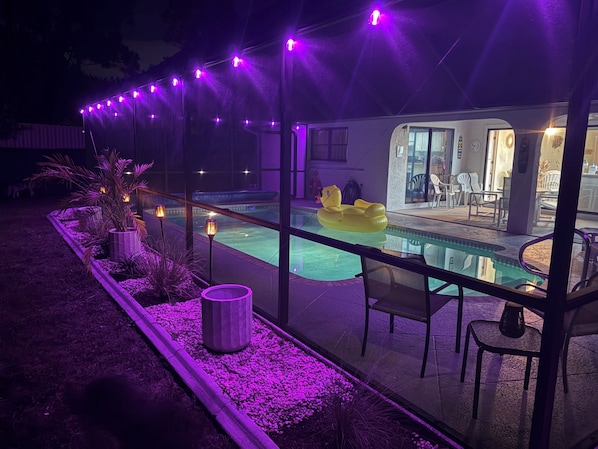 Un'area piscina con barriera in vetro, posti a sedere all'aperto e un galleggiante gonfiabile giallo.