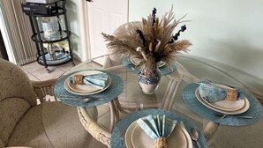 Una mesa de comedor dispuesta con servilletas azules, platos y un jarrón decorativo con plantas secas.