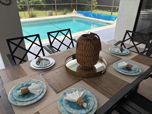 A dining table with a view of a swimming pool, surrounded by chairs.