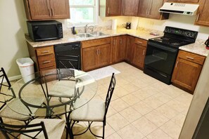 A kitchen with wooden cabinets, a microwave, a dishwasher, a stove, and a glass dining table with chairs. - Sharon A - 8 Bed, Sleeps 11+ (Saint Charles)