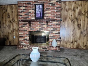 A brick fireplace with a framed picture above it, a vase, and a glass table in front.