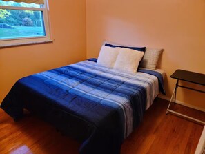 Un dormitorio con cama, ventana y mesita de noche.