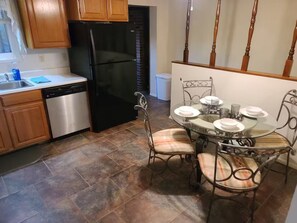 A kitchen with a black refrigerator, wooden cabinets, a dishwasher, and a dining area with a glass table and metal chairs.