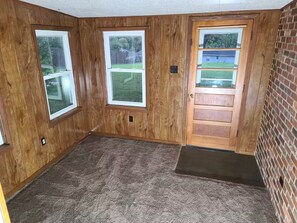 A room with wooden walls, two windows, a door, and a carpeted floor.