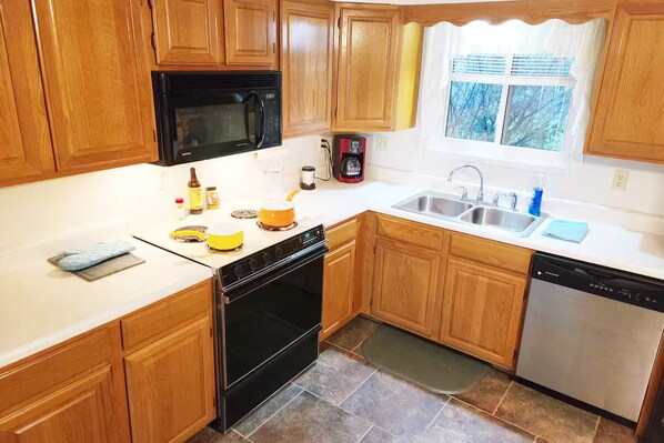 A kitchen with wooden cabinets, a microwave, stove, sink, and dishwasher.