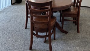 Una mesa de madera redonda con seis sillas, un florero con flores y una planta en maceta en una esquina.
