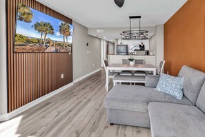 A modern living room with a grey sofa, a dining table with chairs, and a kitchen area with a hanging light fixture. - Aqua Village at Dunes Village (Myrtle Beach)