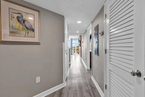A hallway with a framed bird painting, a white door with a window, and a ceiling with recessed lighting. - Aqua Village at Dunes Village (Myrtle Beach)