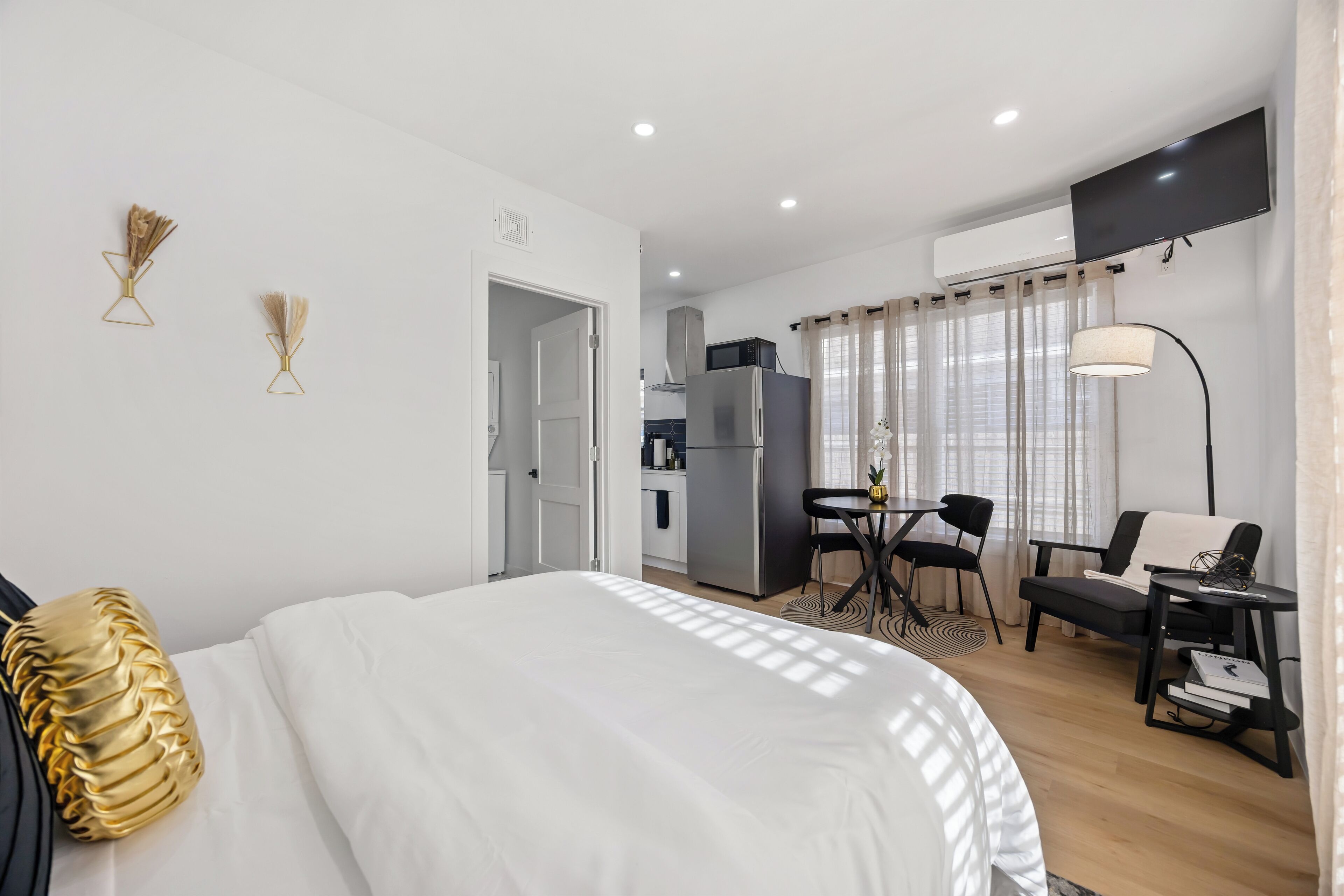 A modern hotel room with a bed, a desk, a chair, a small table, and a TV.