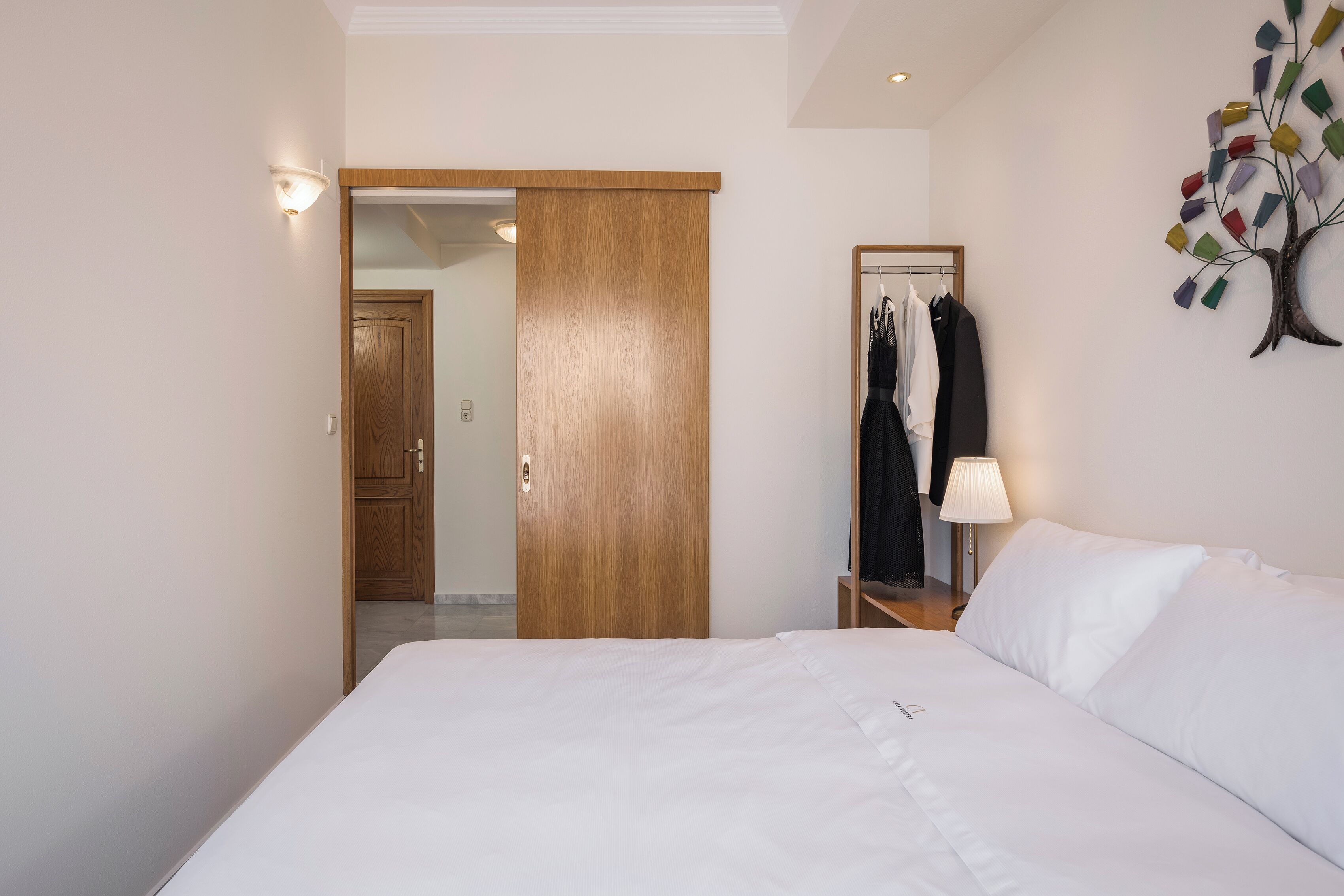 Et hotelværelse med en seng, en trædør, et spejl og en lampe monteret på væggen.