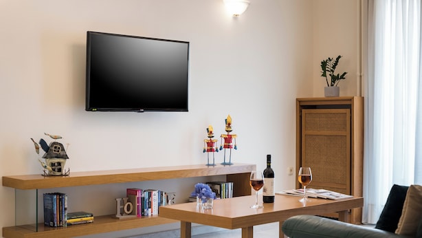 En moderne stue med et fladskærms-tv, træhylder med bøger, dekorative genstande, et bord med et vinglas og et skab i rattan.