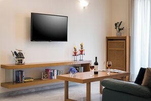 Una sala de estar moderna con un televisor de pantalla plana, estanterías de madera con libros, objetos decorativos, una mesa con una copa de vino y un mueble de mimbre.