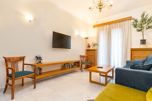 Una sala de estar con sofá, sillas, una mesa de centro, un televisor montado en la pared y una estantería.