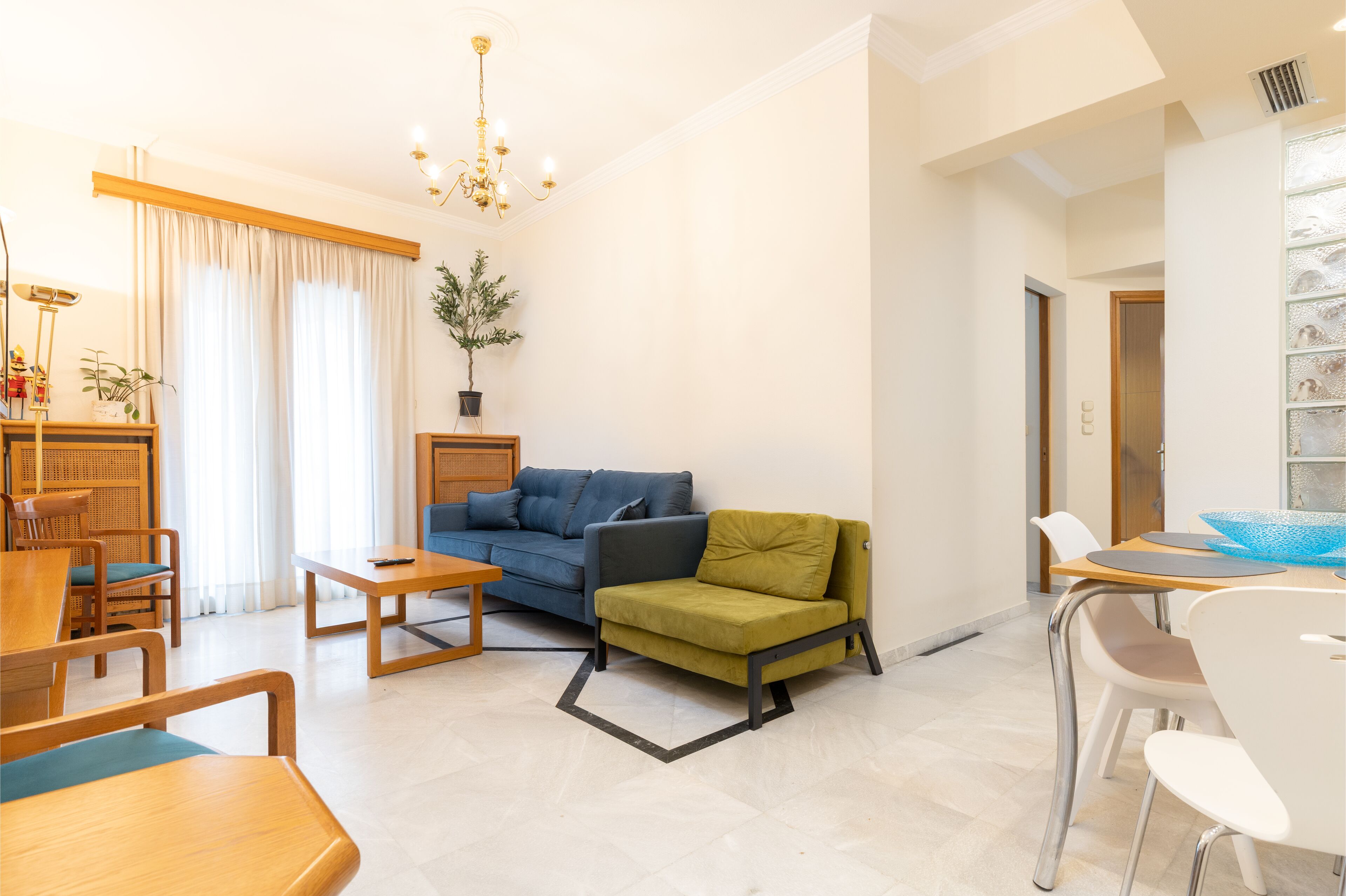 Ein modernes Wohnzimmer mit einem blauen Sofa, einem grünen Sessel, Holzmöbeln und einem Essbereich mit weißen Stühlen.