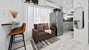 A modern kitchen with a refrigerator, a dining area with a bar stool, and a sofa. - Cityscapes Studio Suite #D @ East Downtown (Houston)