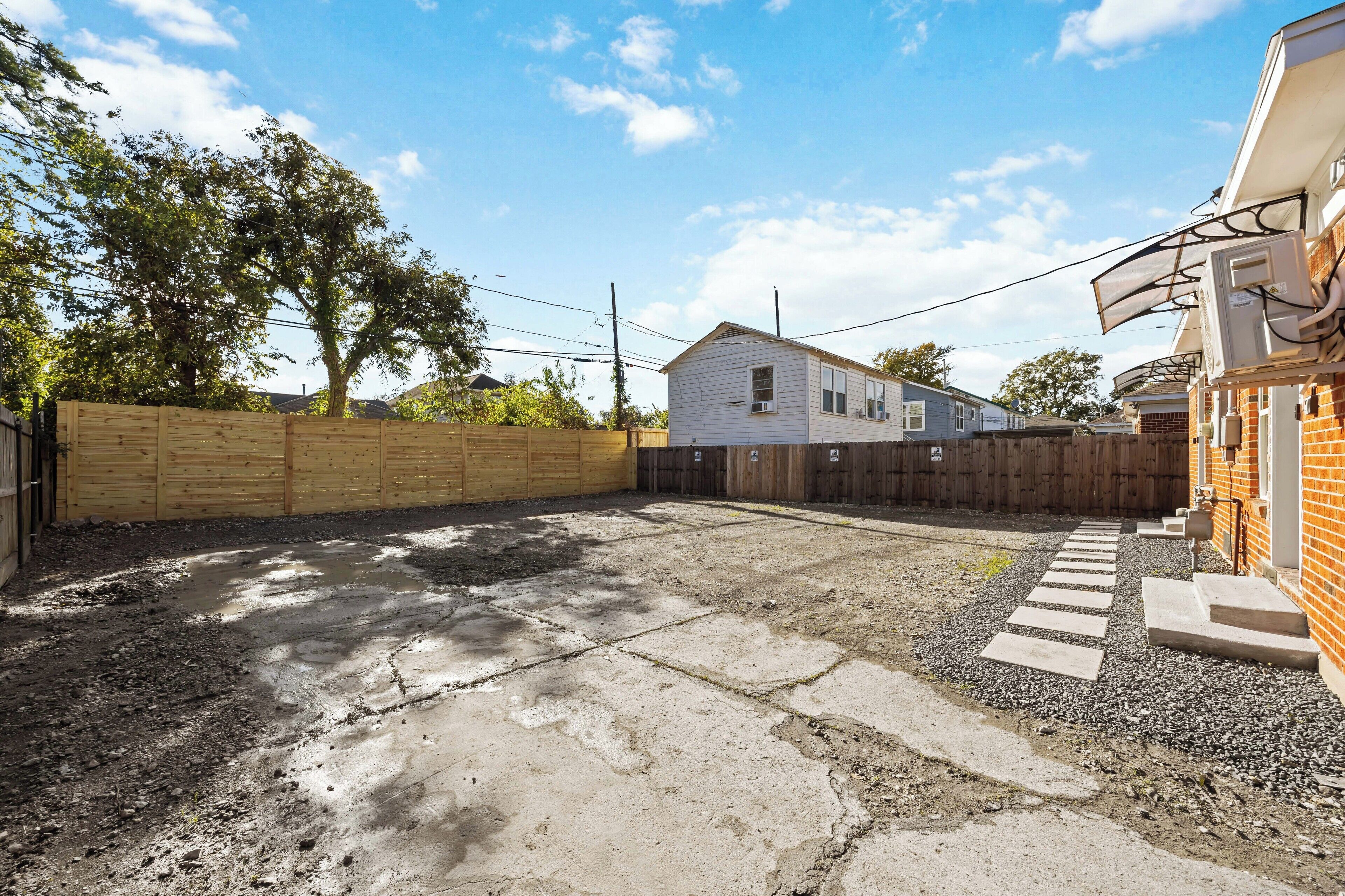 A residential backyard with a concrete patio, wooden fence, and a brick house.