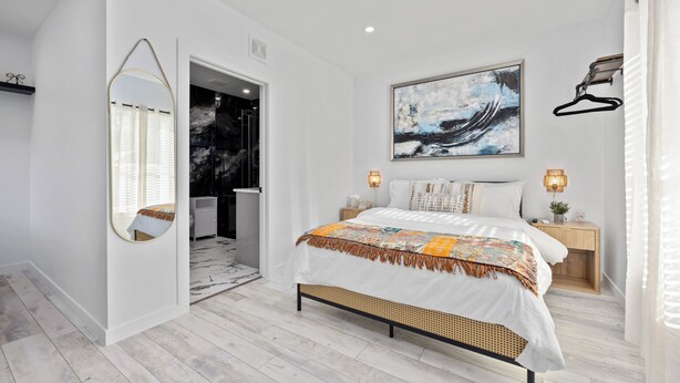 A modern bedroom with a bed, a large mirror, a painting, and a nightstand with a lamp. - Cityscapes Studio Suite #D @ East Downtown (Houston)