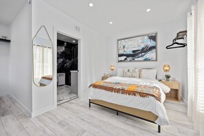 A modern bedroom with a bed, a large mirror, a painting, and a nightstand with a lamp. - Cityscapes Studio Suite #D @ East Downtown (Houston)