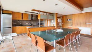 A modern kitchen with a central island, a dining area with a glass table, and wooden cabinets. - Wonderful 5-bedroom villa in Rio Caldo perfect for your getaway (Rio caldo)