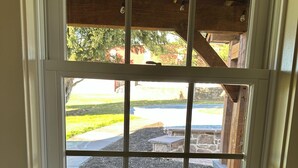 Ventana con diseño enrejado, vigas de madera y vista a un espacio exterior ajardinado con un sendero de piedra y una terraza de madera.