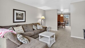 A living room with a sofa, a coffee table, a lamp, and a dining area with chairs and a table.