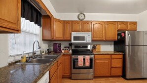 A kitchen with wooden cabinets, a stainless steel refrigerator, a microwave, a stove, and a clock on the wall.