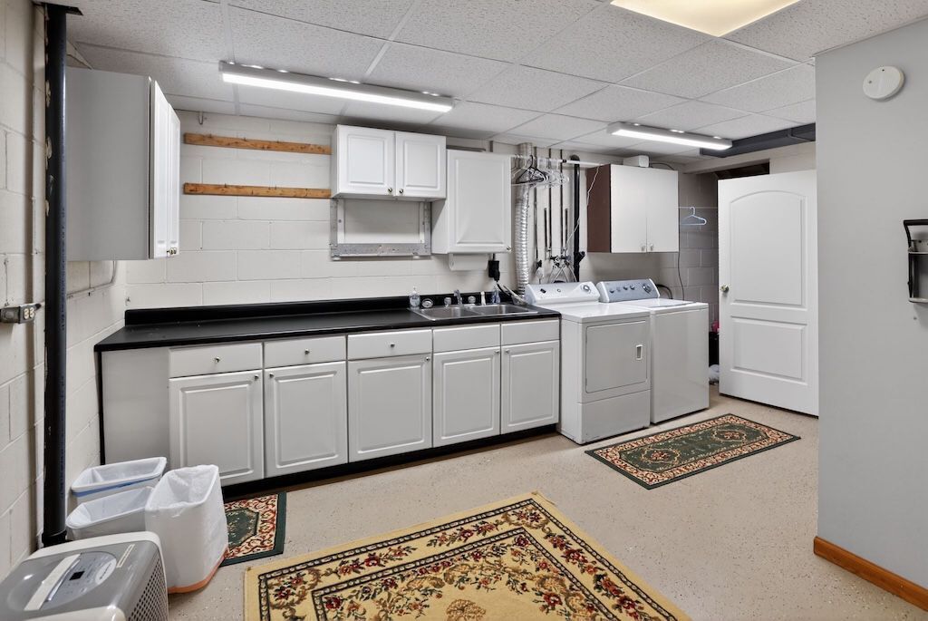 A compact kitchen with white cabinets, a black countertop, and a built-in oven. There are two rugs on the floor, and a white door is visible in the background.