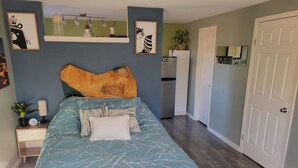 Ein Schlafzimmer mit einem großen Bett, einem Nachttisch mit Lampe, einer Kommode und einer Tür.
