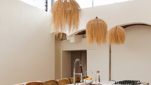 A modern kitchen with a marble island, wooden chairs, a gas stove, and a hanging light fixture. - Oasis with Swimming Pool in the Heart of Oaxaca (Oax.)