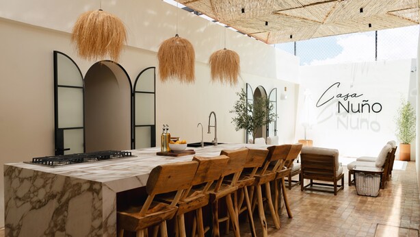 A modern kitchen with a marble island, wooden chairs, hanging light fixtures, and a large window with a view. - Oasis with Swimming Pool in the Heart of Oaxaca (Oax.)