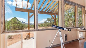 Habitació amb grans finestres, un telescopi sobre un trípode i vista a un paisatge muntanyós.