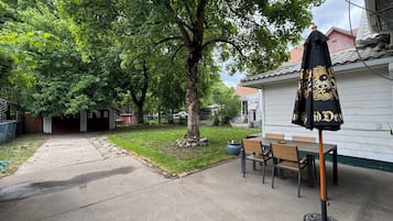 Une terrasse avec une table et des chaises, un parasol noir et un arbre.