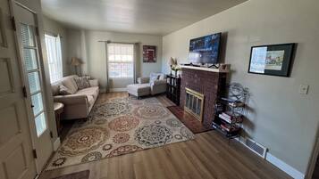 A living room with a fireplace, a television mounted above it, and a large rug on the floor.