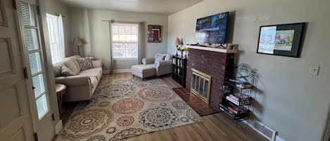 A living room with a fireplace, a television mounted above it, and a large rug on the floor.