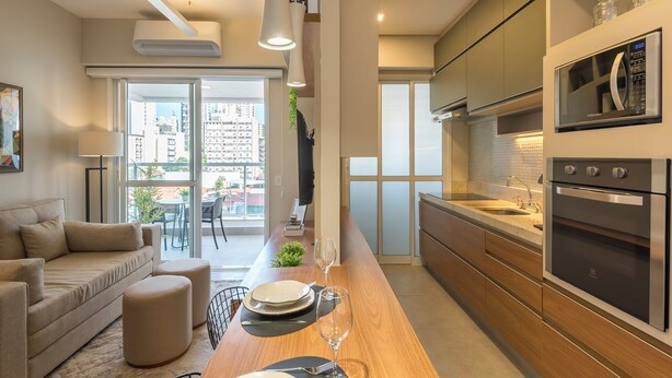 A modern kitchen with a built-in oven, a dining area with a table set for two, and a sofa in the living area. - Modern Apartment in Cambuí (Campinas)