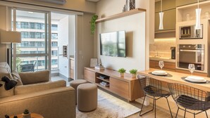 A modern apartment with a living room, kitchen, and dining area. It features a large window, a flat-screen TV, a wooden dining table with chairs, and a built-in oven. - Modern Apartment in Cambuí (Campinas)