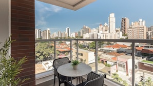 A balcony with a table and chairs, a potted plant, and a city view. - Modern Apartment in Cambuí (Campinas)