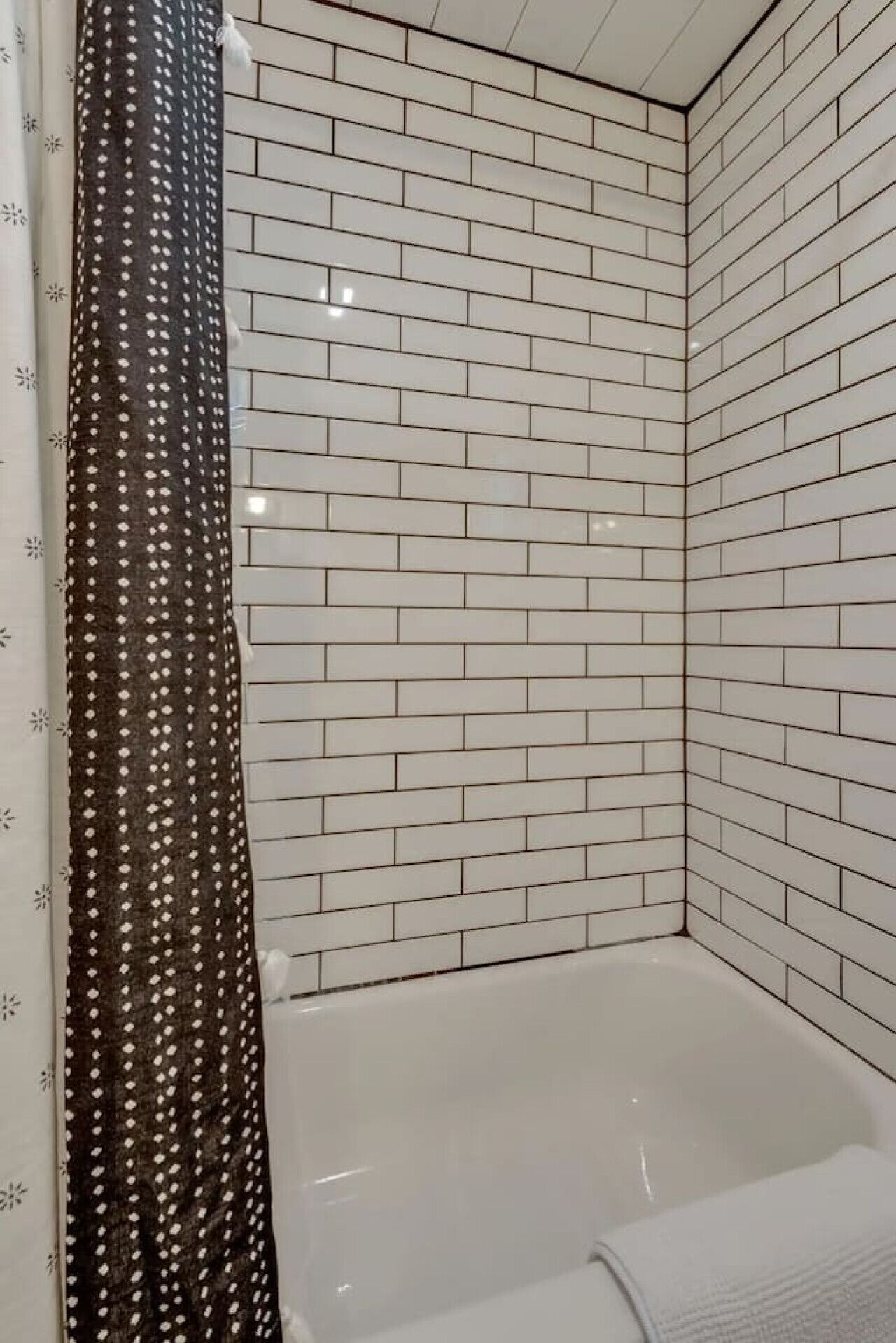 Un baño con azulejos tipo metro blancos, una bañera blanca y una cortina de ducha estampada.