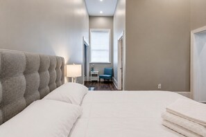 A bedroom with a large bed, a bedside table, a lamp, a chair, and a window with blinds.