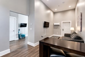 Un salon moderne avec une table à manger en bois foncé, un canapé gris, un téléviseur à écran plat fixé au mur et une porte blanche.