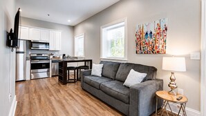 A modern kitchen with stainless steel appliances, a gray sofa, and a wooden floor. - Bright & Cozy Church Conversion • 1BR (Nashville)