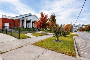 A building with a brick facade and a white entrance, surrounded by a sidewalk and a small tree with autumn leaves. - Historic Church Loft | East Nash | Free Parking (Nashville)