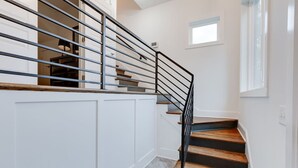 Eine Treppe mit Metallgeländer, Holzstufen und einer weißen Wand mit einem kleinen Fenster.